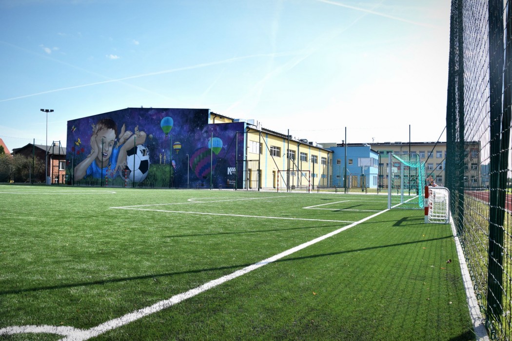 Boisko do piłki nożnej , budynek nowej sali sportowej z namalowanym rysunkiem małego chłopca z piłką 