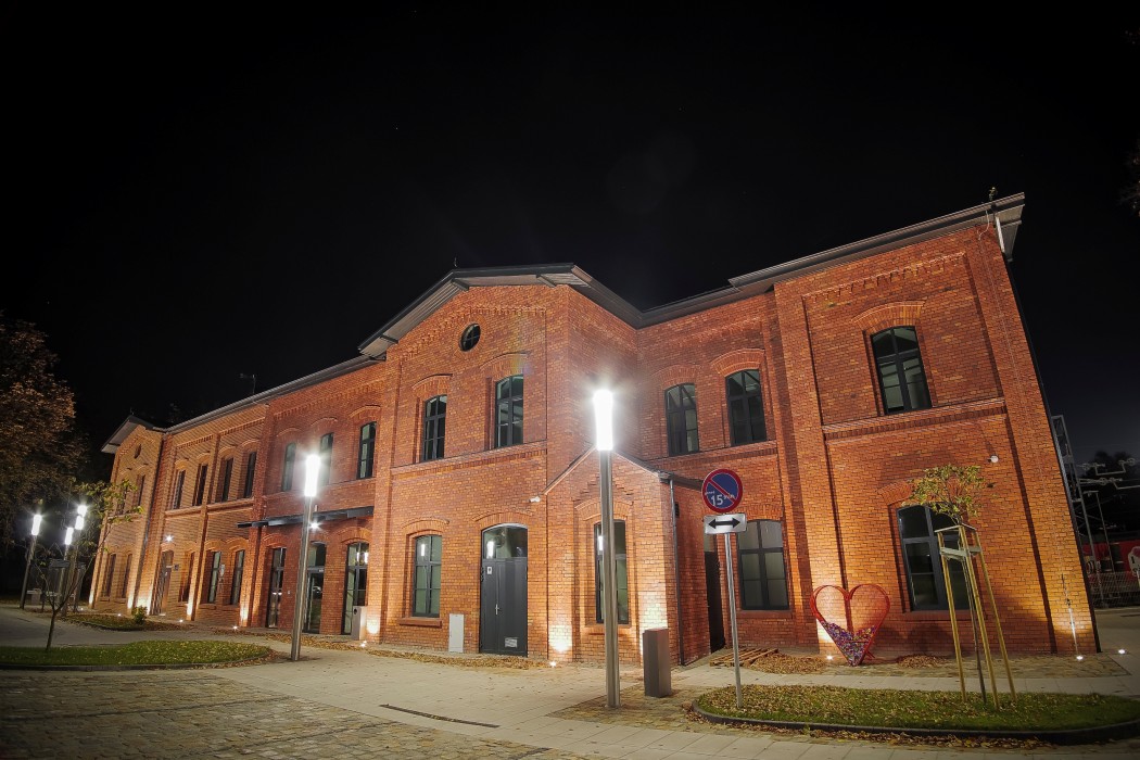 Budynek dworca PKP w Żorach. Zdjęcie zrobione w nocy od frontu budynku. Na pierwszym planie latarnie oświetlające budynek i wejście na Dworzec. 