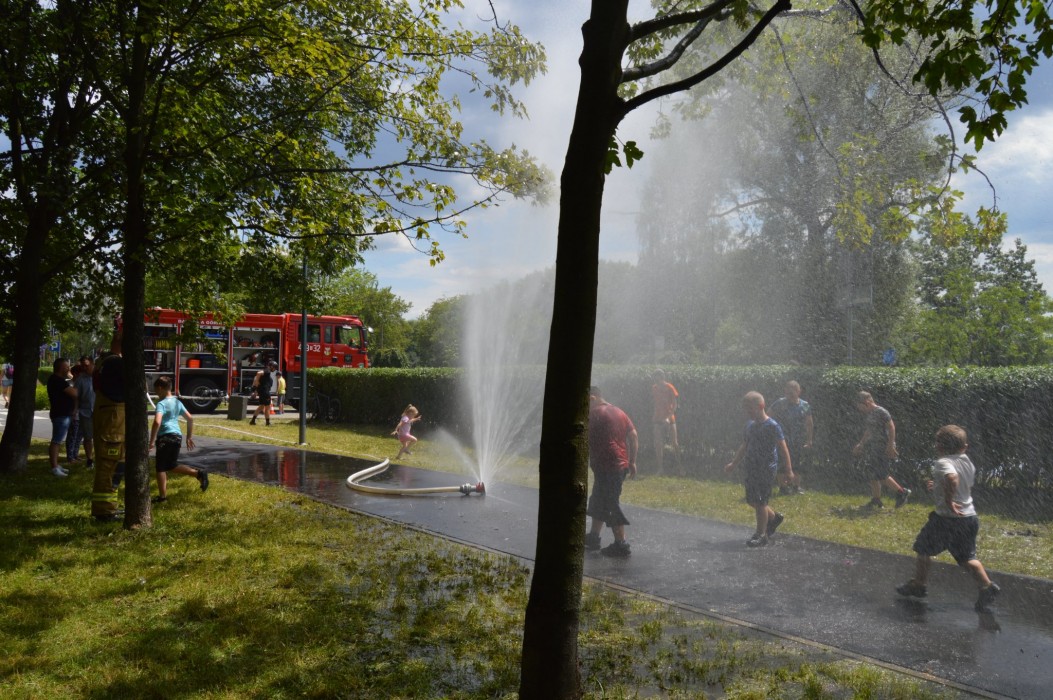 Dzieci bawiące się w wodzie tryskającej z węża strażackiego. 