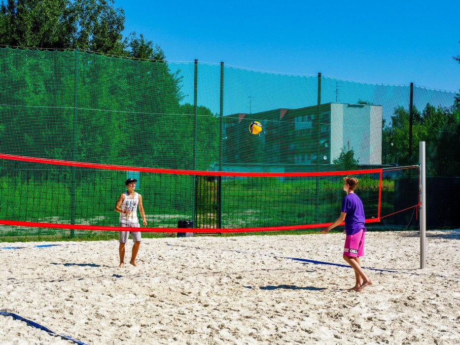 Boisko do piłki siatkowej plażowej w słoneczny dzień. Na boisku dwaj chłopcy, grający w siatkówkę plażową. 