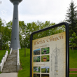 Nitowana wieża ciśnień w Będzinie-Grodźcu. Na pierwszym planie wybrukowany plac z tablicą informacyjną przedstawiającą wieżę ciśnień przed i po renowacji. W tle, na skarpie, otoczona wysokimi drzewami 