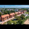Zdjęcie wykonane z drona, obejmujące 5 zrewitalizowanych budynków kolonii robotniczej Hugon wraz z terenem wokół na którym znajduje się m.in. parking. Na drugim planie budynki mieszkalne w Rojcy. 