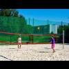 Boisko do piłki siatkowej plażowej w słoneczny dzień. Na boisku dwaj chłopcy, grający w siatkówkę plażową. 