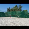 Boisko do siatkówki plażowej, na którym widoczni są dwaj chłopcy grający w siatkówkę. Boisko otoczone płotem z siatki. 