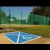 Na pierwsyzm planie widoczne miejsce parkingowe dla osób z niepełnosprawnościami. W tle widoczne boisko do piłki siatkowej. 