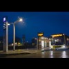 Nowoczesny przystanek autobusowy wieczorową porą w deszczu. Podświetlony delikatnym światłem. Na jednym z peronów żółty autobus przegubowy marki MAN z wyświetloną nazwą przystanku "ŚWIERKLANIEC PARK". 