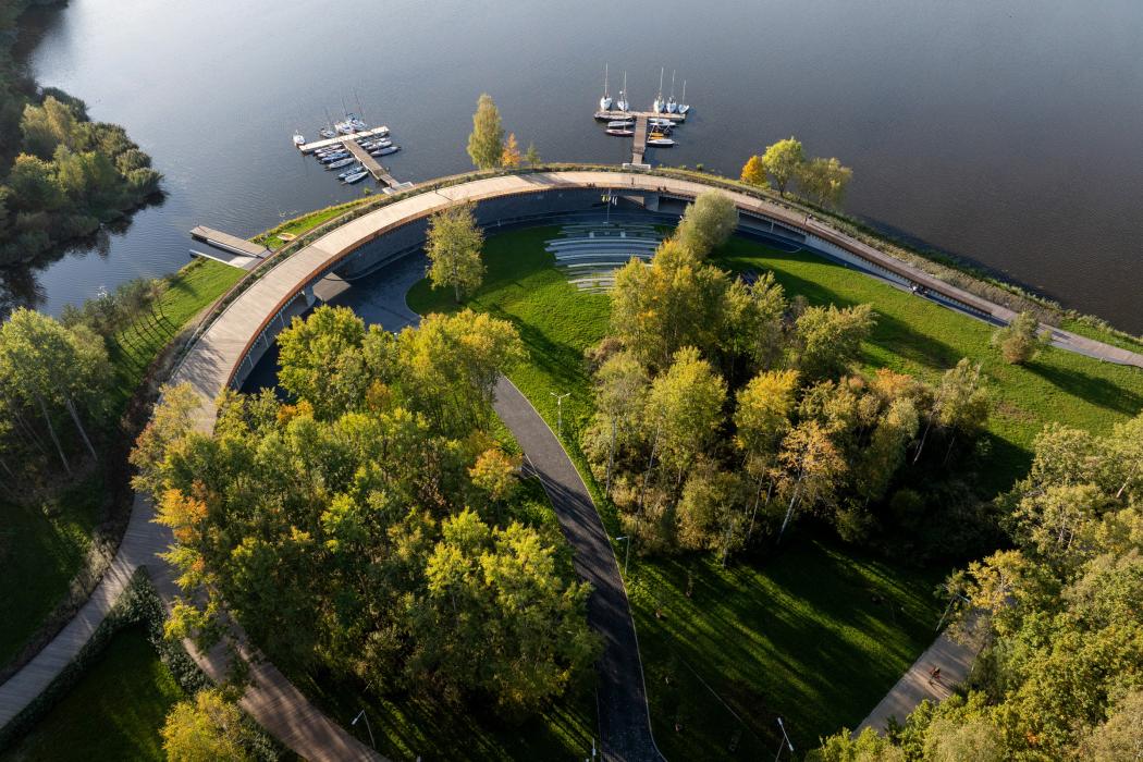 Widok z góry na marinę ukazujący budynek pod promenadą oraz pomosty dla łodzi wkomponowane w istniejącą zieleń 
