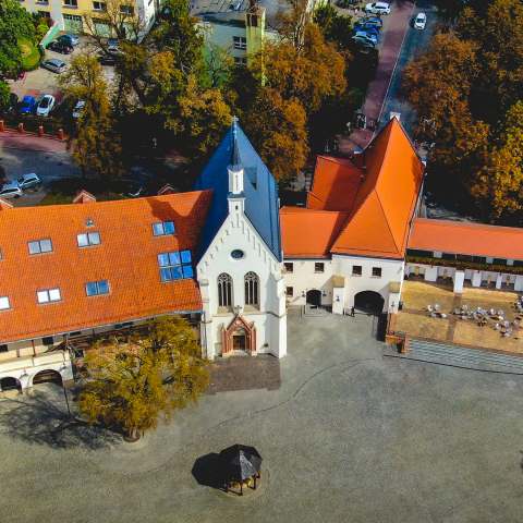 Widok z lotu ptaka na część wschodnią połączonych zabudowań zamku Piastowskiego w Raciborzu – w centralnej części zdjęcia od lewej: dom książęcy, gotycka kaplica, budynek bramny i baszta. Nad zabudowaniami w tle zieleń. Poniżej zabudowań dziedziniec ze studnią i drzewem.