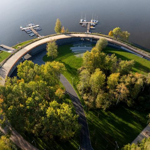 Widok z góry na marinę ukazujący budynek pod promenadą oraz pomosty dla łodzi wkomponowane w istniejącą zieleń 