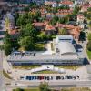 Widok budynku z lotu ptaka, budynek o prostokątnym obrysie i jasno szarym płaskim dachu, otoczony chodnikiem, trawnikami i drzewami, przed budynkiem, równolegle do elewacji biegnie ulica i znajduje się parking.