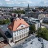 Widok z lotu ptaka w perspektywie, na tle miasta. Na pierwszym planie wyremontowany, zabytkowy budynek spinPLACE. W tle panorama wschodniej części śródmieścia Katowic z zabudową przy ul. Warszawskiej, neogotycką, kamienną wieżą kościoła przy ulicy  Mariackiej. Na ostatnim planie, w oddali osiedle budynków wielorodzinnych oraz żurawie budowlane.
