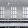 Sala konferencyjna. W pomieszczeniu pierwszym planie stoły i krzesła ułożone w układzie konferencyjnym, wokół prostokąta. W tle ściana z trzema dużymi oknami o zabytkowym charakterze, przez które widoczne są budynki po drugiej stronie ulicy. Po lewej fragment ściany z dużym, nowoczesnym przeszkleniem.