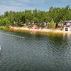 Skarpa jeziora od strony wody, z widoczną wzdłuż brzegu piaszczystą plażą. Z lewej strony płynie żaglówka, Z prawej strony magazyn sprzętu ratowników z tarasem widokowym na dachu oraz trzy szeregi gabionów z szarego granitu. Na dalszym planie biały budynek, parasole i ludzie. 