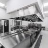 Profesjonalna kuchnia zbiorowego żywienia wyposażona w stalowe ciągi technologiczne, okapy wentylacyjne oraz urządzenia gastronomiczne zapewniające higieniczne i funkcjonalne warunki przygotowywania posiłków