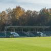 Boisko piłkarskie z naturalną nawierzchnią w Parku Sportowym w Wojkowicach i zadaszoną trybuną w tle.