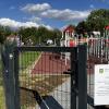 Wejście na teren placu zabaw w Dzięgielowie wraz z tablicą informującą o realizacji inwestycji współfinansowanej ze środków Województwa Śląskiego w ramach programu „Inicjatywa Sołecka”. W tle widoczne urządzenia zabawowe oraz ogrodzony teren rekreacyjny.