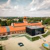 Widok z lotu ptaka na zrewitalizowaną cechownię dawnej kopalni „Saturn” w Czeladzi. Historyczny ceglany budynek połączono z nowoczesną przeszkloną częścią, a wokół urządzono parking, tereny zielone i przestrzeń rekreacyjną.