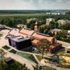 Widok z lotu ptaka na zrewitalizowany kompleks dawnej kopalni „Saturn” w Czeladzi. Historyczna cechownia z wieżą zegarową sąsiaduje z nowoczesną Mediateką, a wokół znajdują się parking, tereny zielone i plac zabaw o industrialnym charakterze.