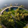 Widok z góry na marinę ukazujący budynek pod promenadą oraz pomosty dla łodzi wkomponowane w istniejącą zieleń 