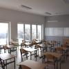 Nowoczesna klasa szkolna z rzędami ławek i krzeseł skierowanymi w stronę dużej tablicy. Widać duże, wysokie okna.